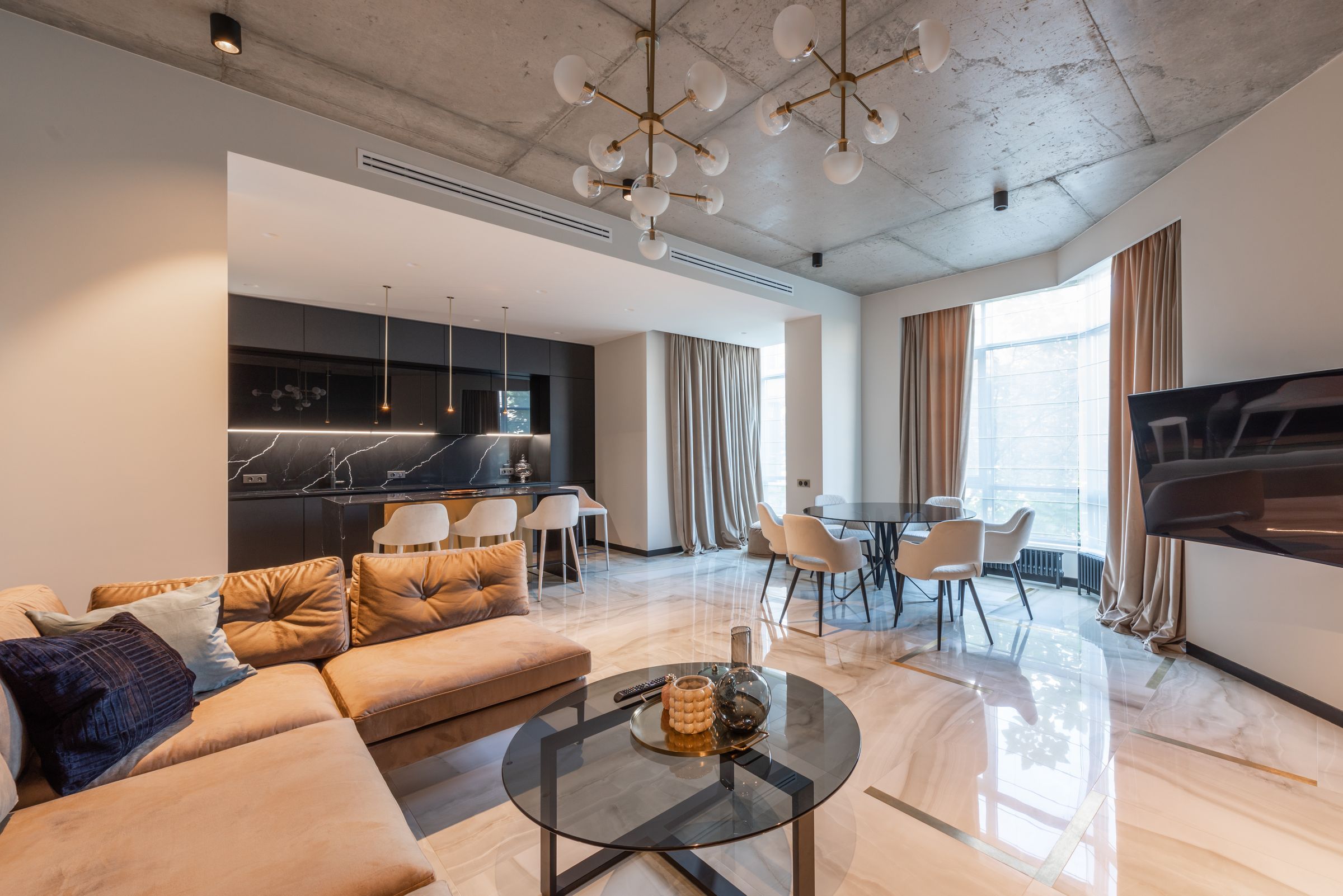 Living room with a caramel velvet sectional, round glass table and a concrete ceiling