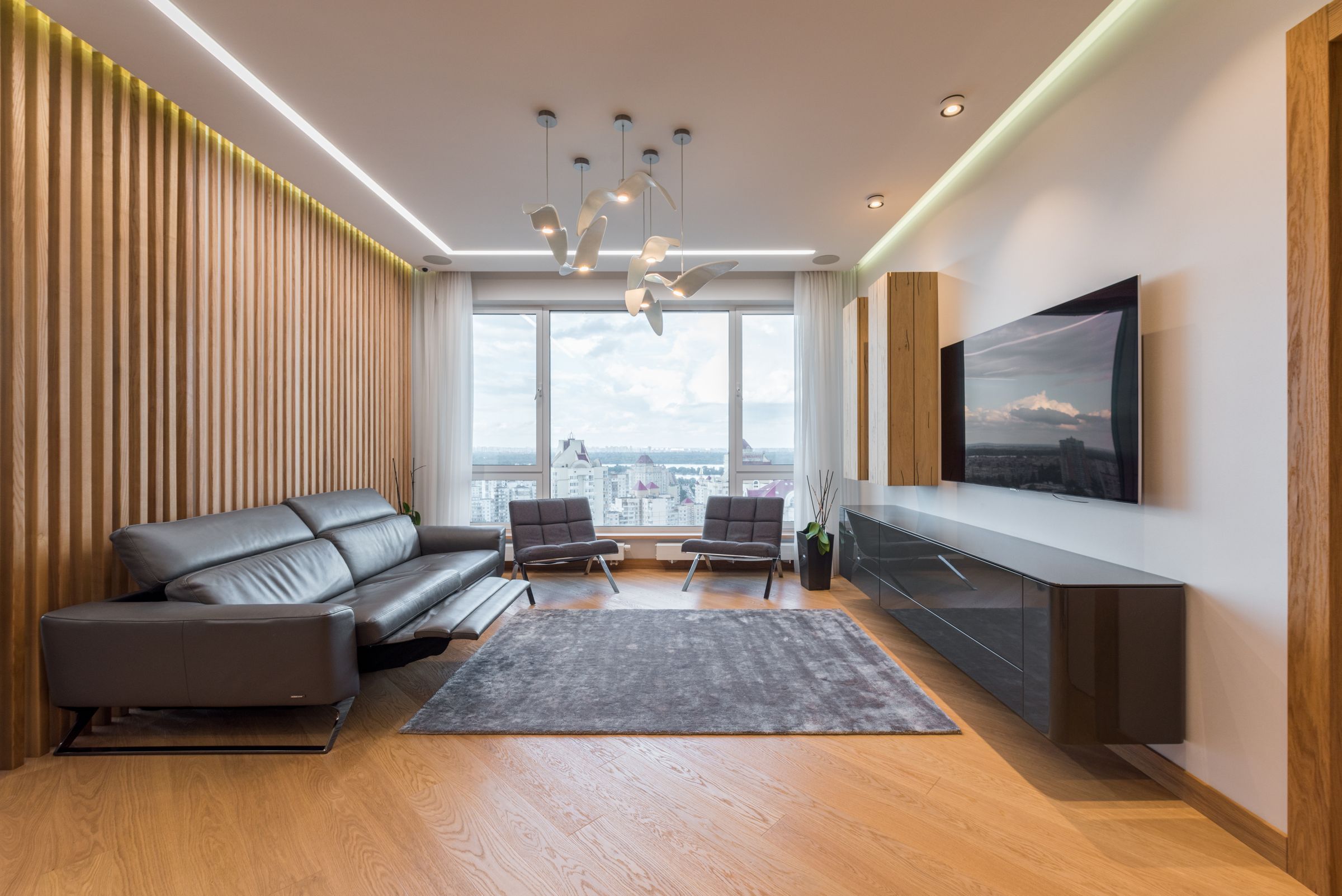 Living room with an oak slat wall, charcoal leather sofa and floor-to-ceiling windows over Queens