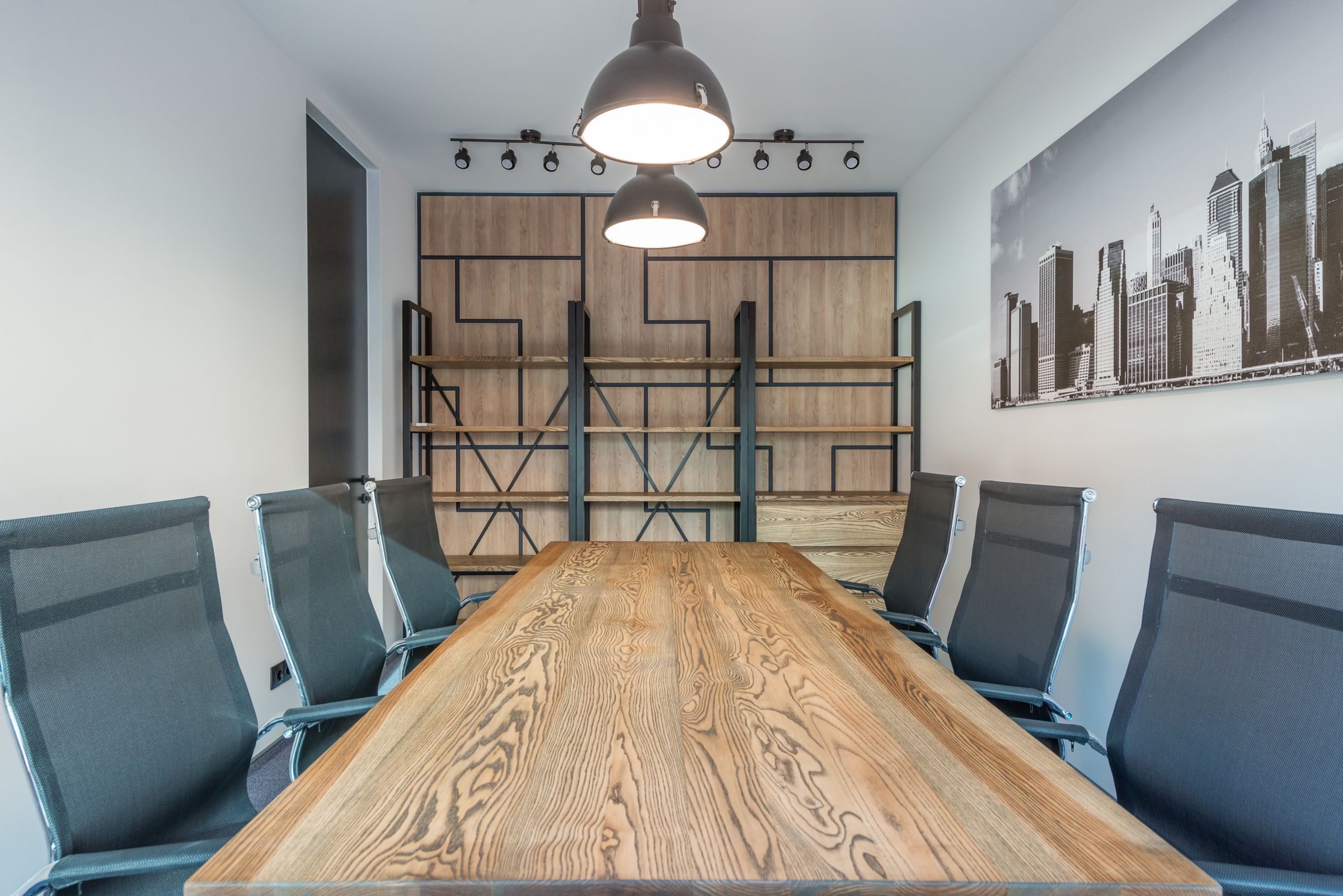 Meeting room with a long ash table, mesh chairs and industrial pendant lights