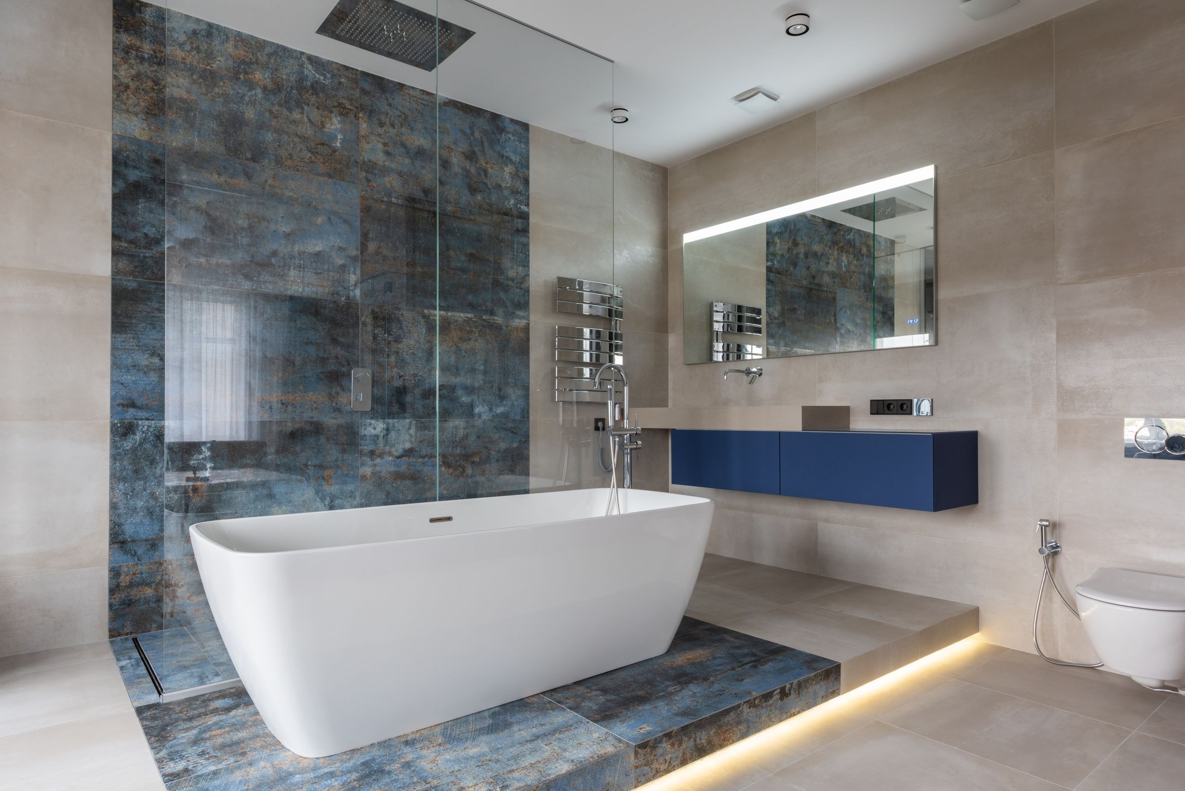 Freestanding tub in front of a blue-veined stone wall with a rain shower