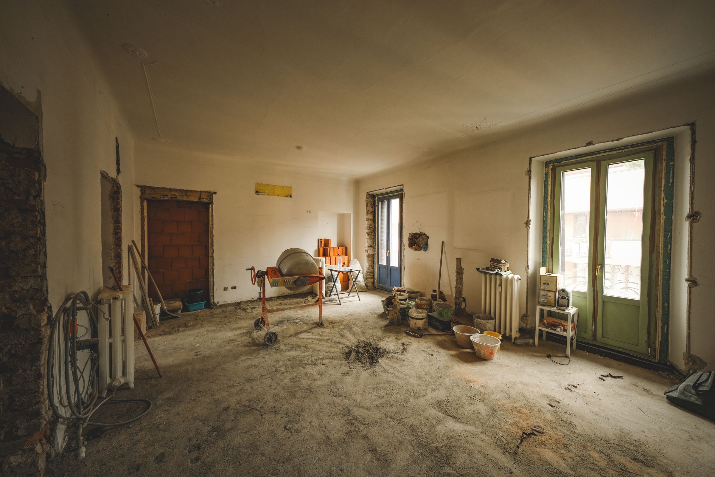 Main floor during demolition, with bare plaster walls, a cement mixer and building materials