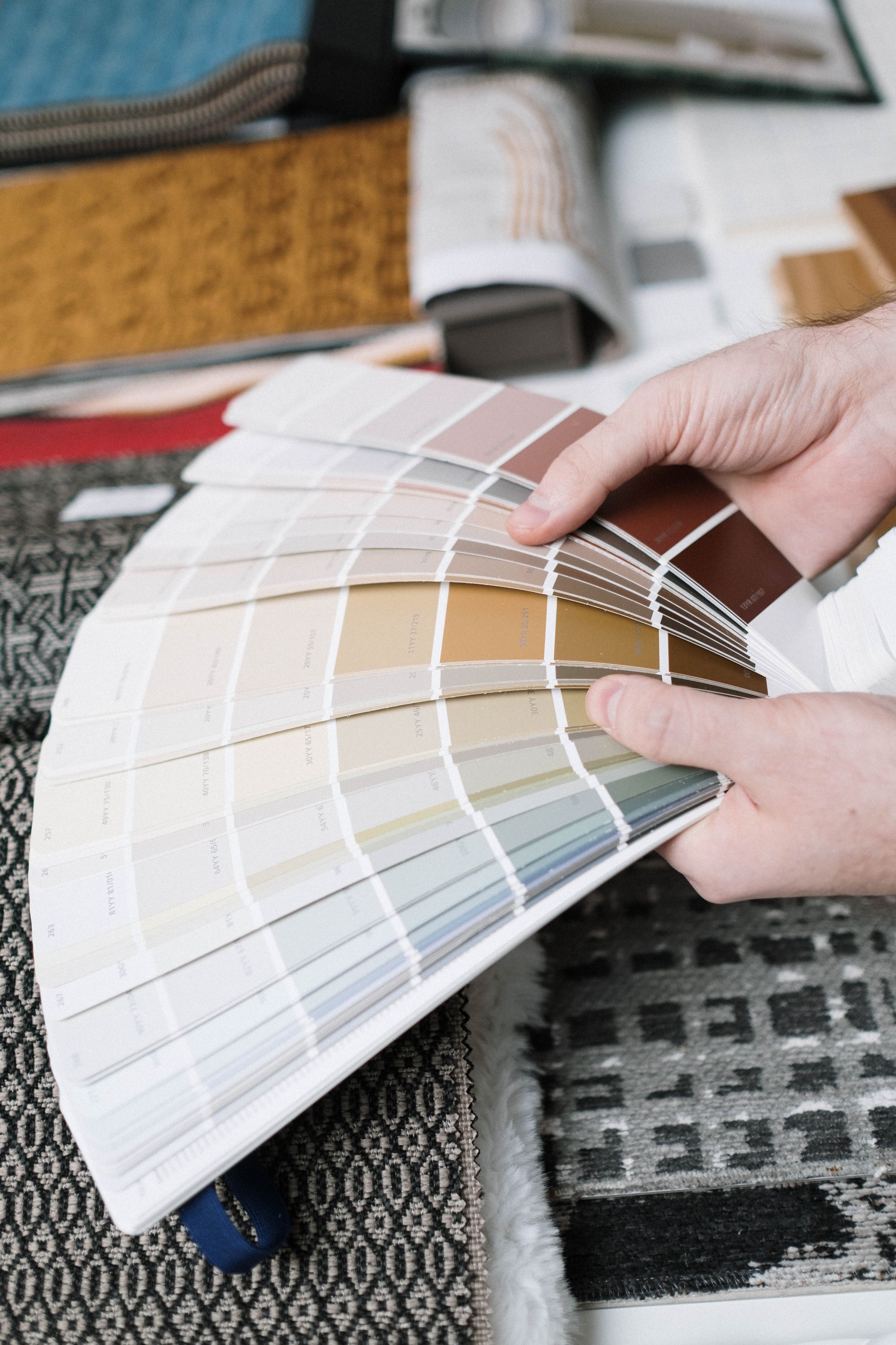 Hands fanning out a paint deck of whites and pale neutrals over fabric samples